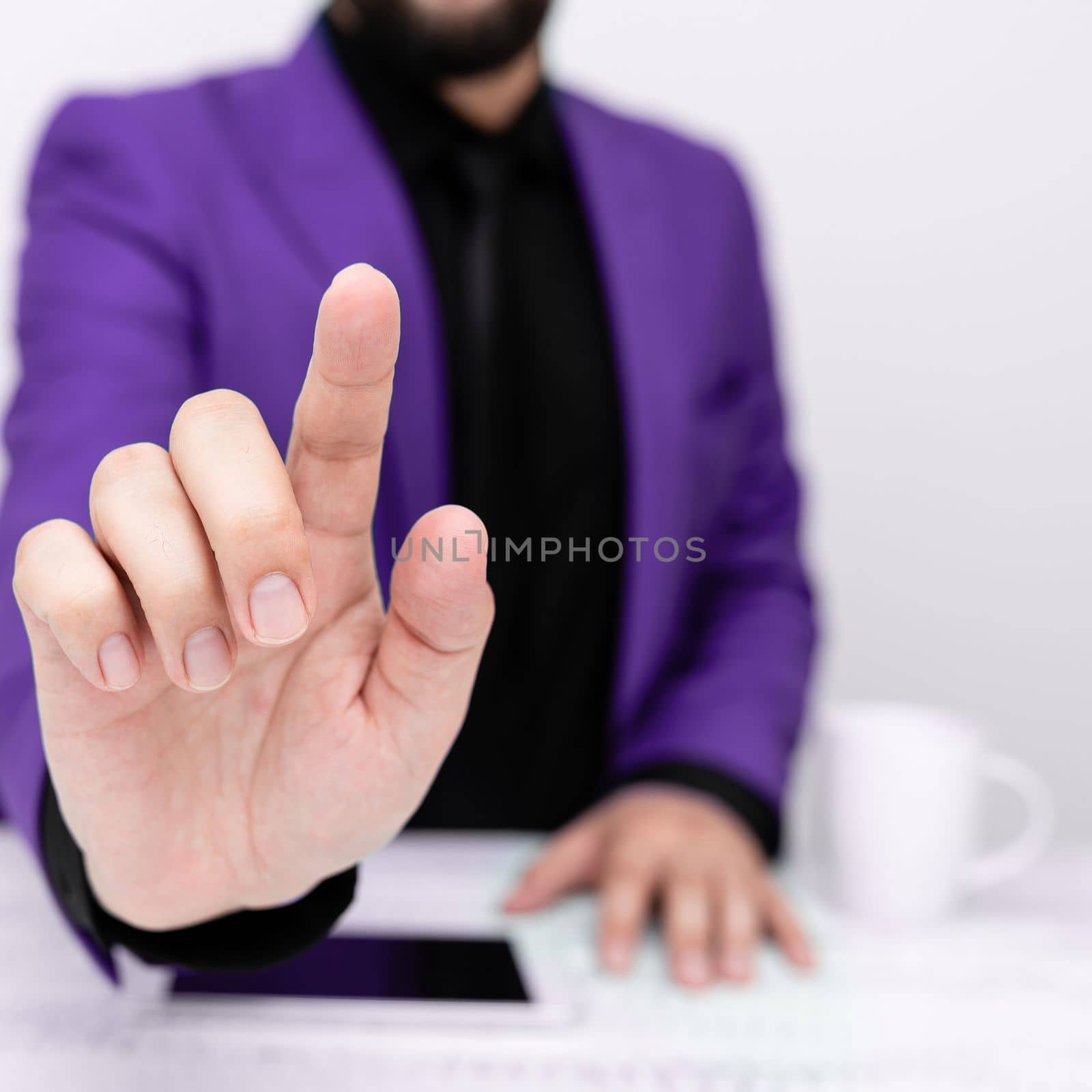 Businessman in Purple jacket sitting at table And Pointing With One Finger On Important Message. Gentleman Showing Critical Announcement. Phone on table. by nialowwa