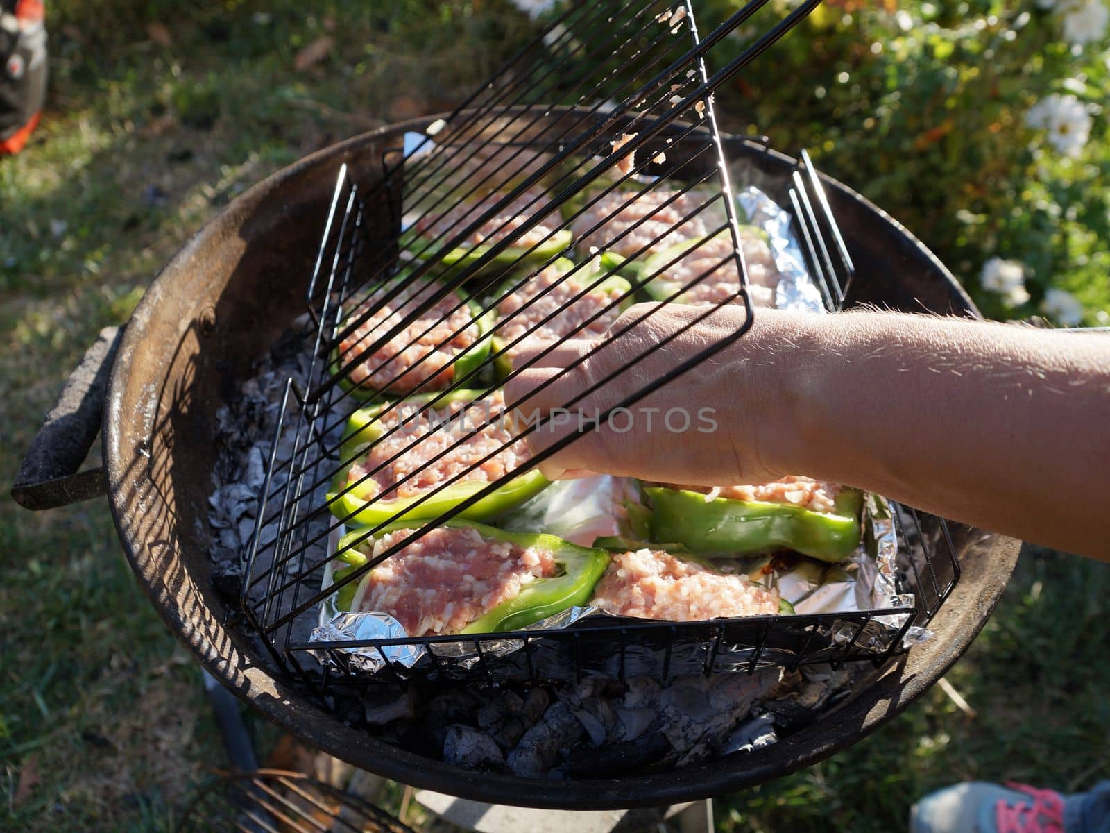 hand stacks stuffed peppers on the grill close-up by Annado