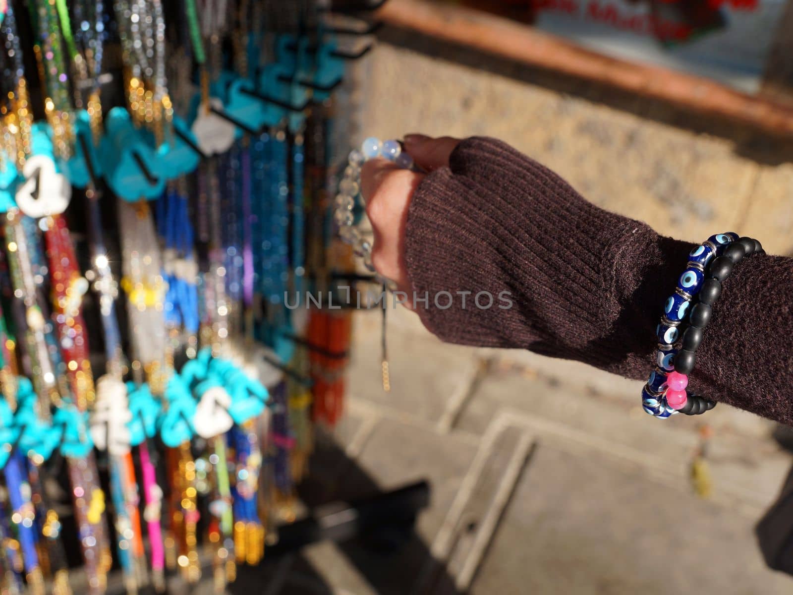 a woman's hand chooses a bracelet at a street bazaar in the sunlight by Annado