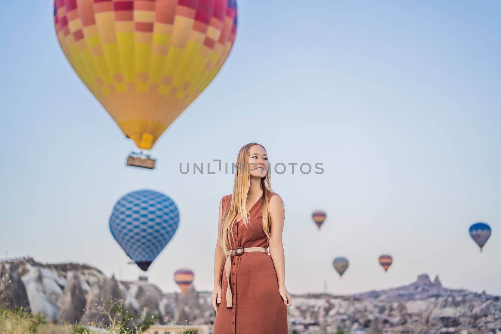 Tourist woman looking at hot air balloons in Cappadocia, Turkey. Happy Travel in Turkey concept. Woman on a mountain top enjoying wonderful view.