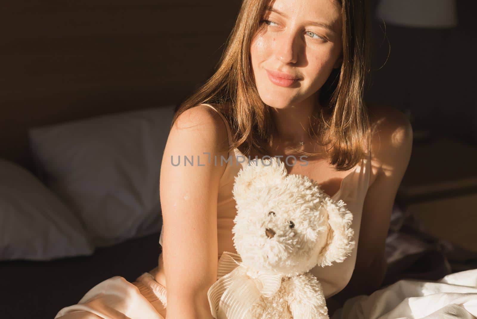 Portrait woman waking up in her bed, she is smiling and stretching with toy bear. Happy young woman greets new sunny day by Satura86