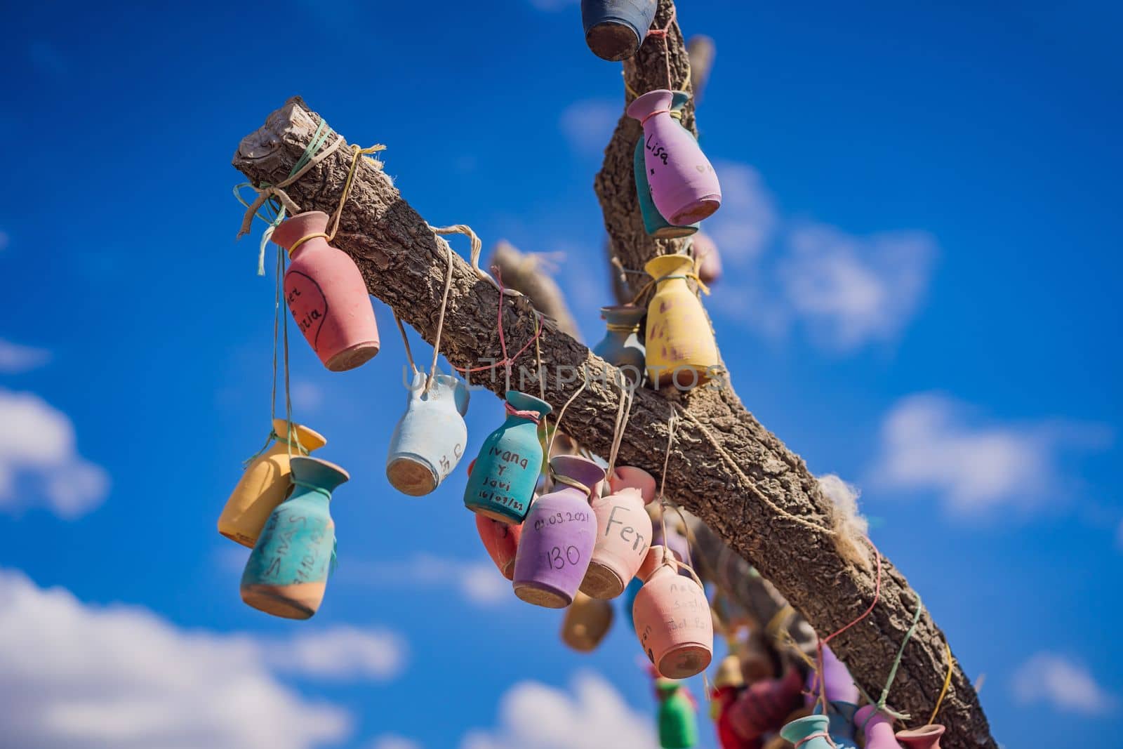 Wish tree. Small multi-colored jugs with inscriptions, wishes hanging on the branches of a tree., against the backdrop of sand ruins and blue sky.