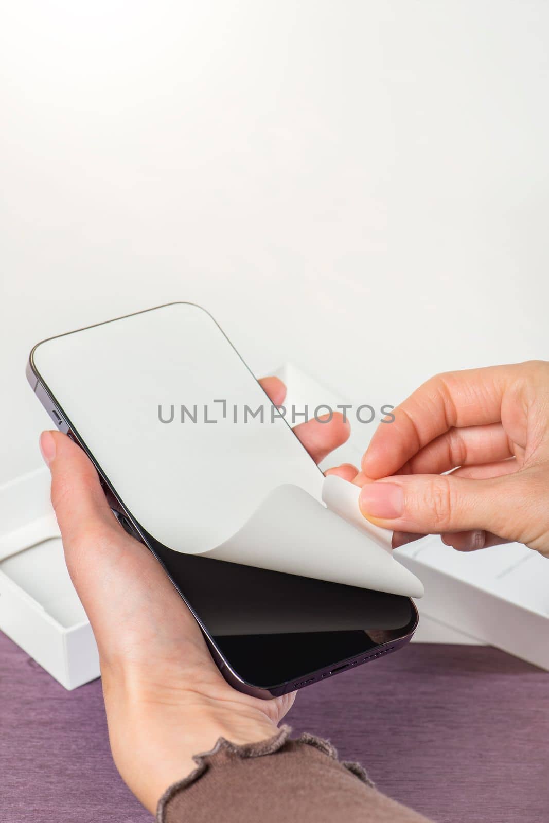 Unpacking a new phone. Remove the protective white film from the new phone. Close-up of a woman's hands removing a protective film from a phone in a purple case. Copy space on white background