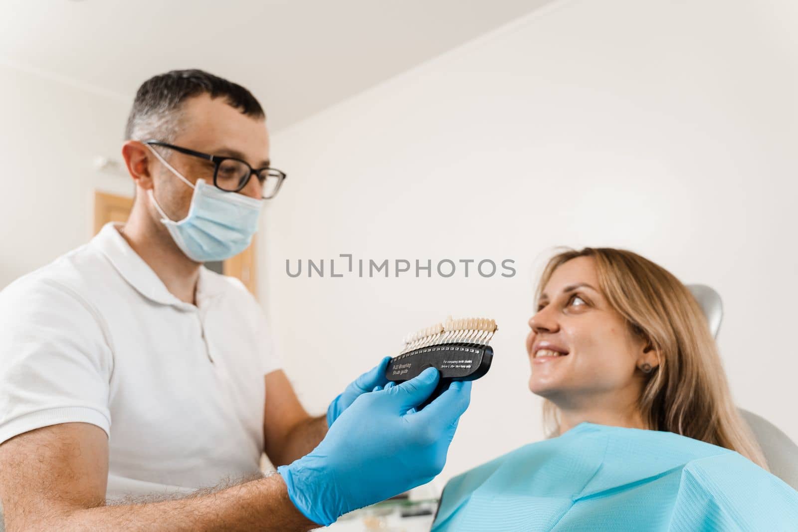 Dentist demonstrate teeth color shades guide for tooth whitening for woman patient in dental clinic. Dentistry. Woman looking at veneers or implants teeth color matching samples in doctor hands