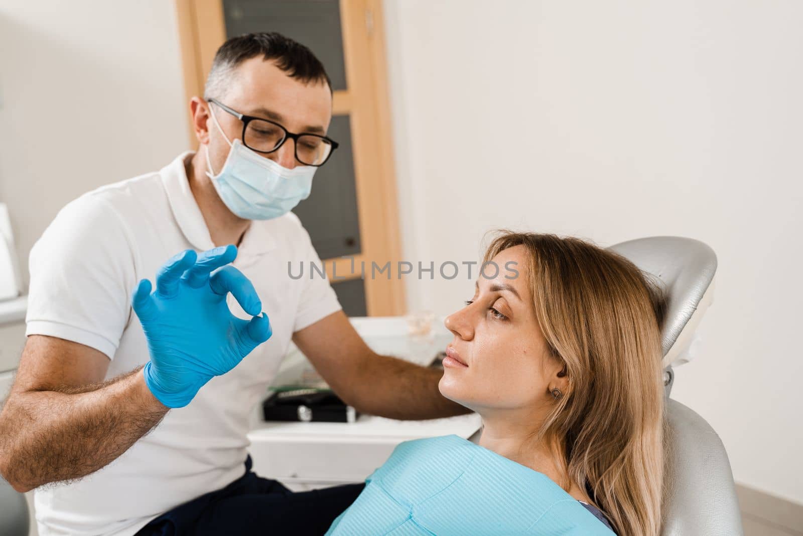 Dentist showing dental veneer teeth implant to woman patient in dental clinic. Dentistry. Consultation with dentist about tooth implantation and whitening