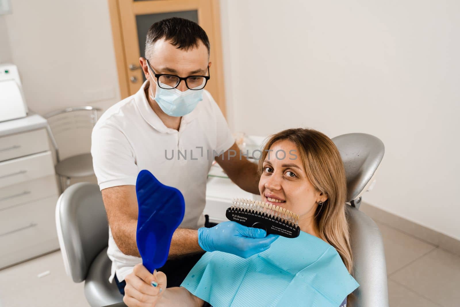 Teeth whitening. Patient looking at teeth color shades guide. Dentistry. Doctor checking tooth color matching samples in dental clinic. by Rabizo