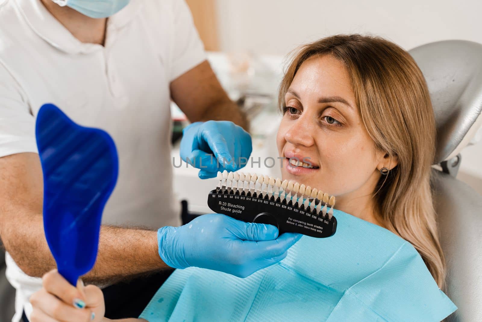 Teeth whitening. Dentist working with teeth color shades guide. Patient looking in mirror. Dentistry. Doctor checking teeth color matching samples in dental clinic