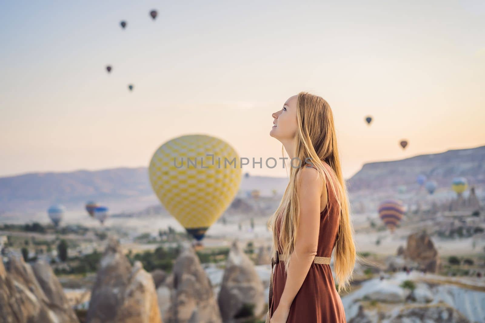 Tourist woman looking at hot air balloons in Cappadocia, Turkey. Happy Travel in Turkey concept. Woman on a mountain top enjoying wonderful view.
