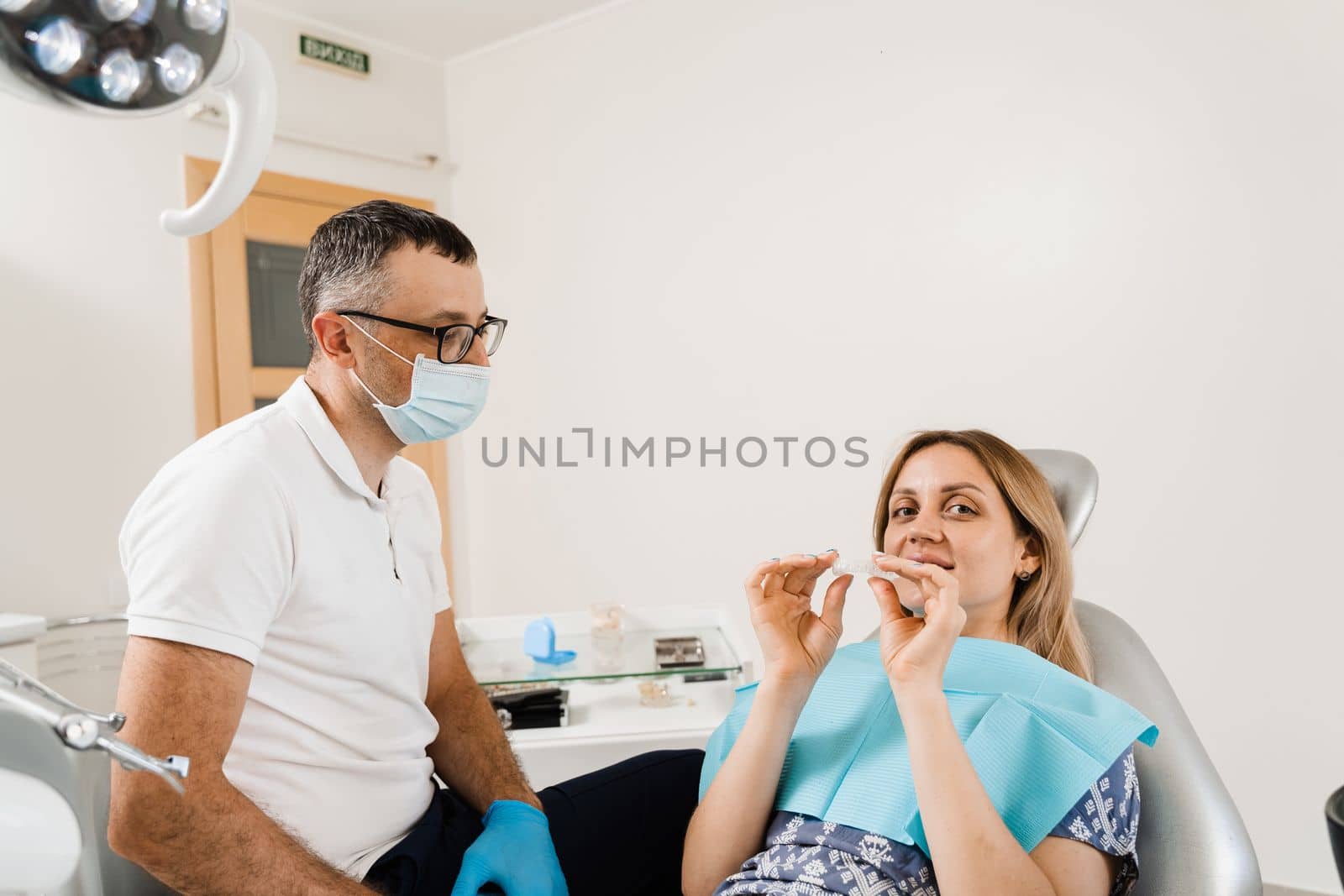Dentist consult woman about using removable clear braces aligner, orthodontic silicone trainer. Portrait girl with white smile using invisible whitening tray. Smiling woman with healthy teeth