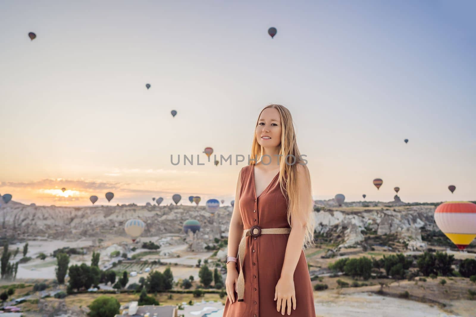 Tourist woman looking at hot air balloons in Cappadocia, Turkey. Happy Travel in Turkey concept. Woman on a mountain top enjoying wonderful view.