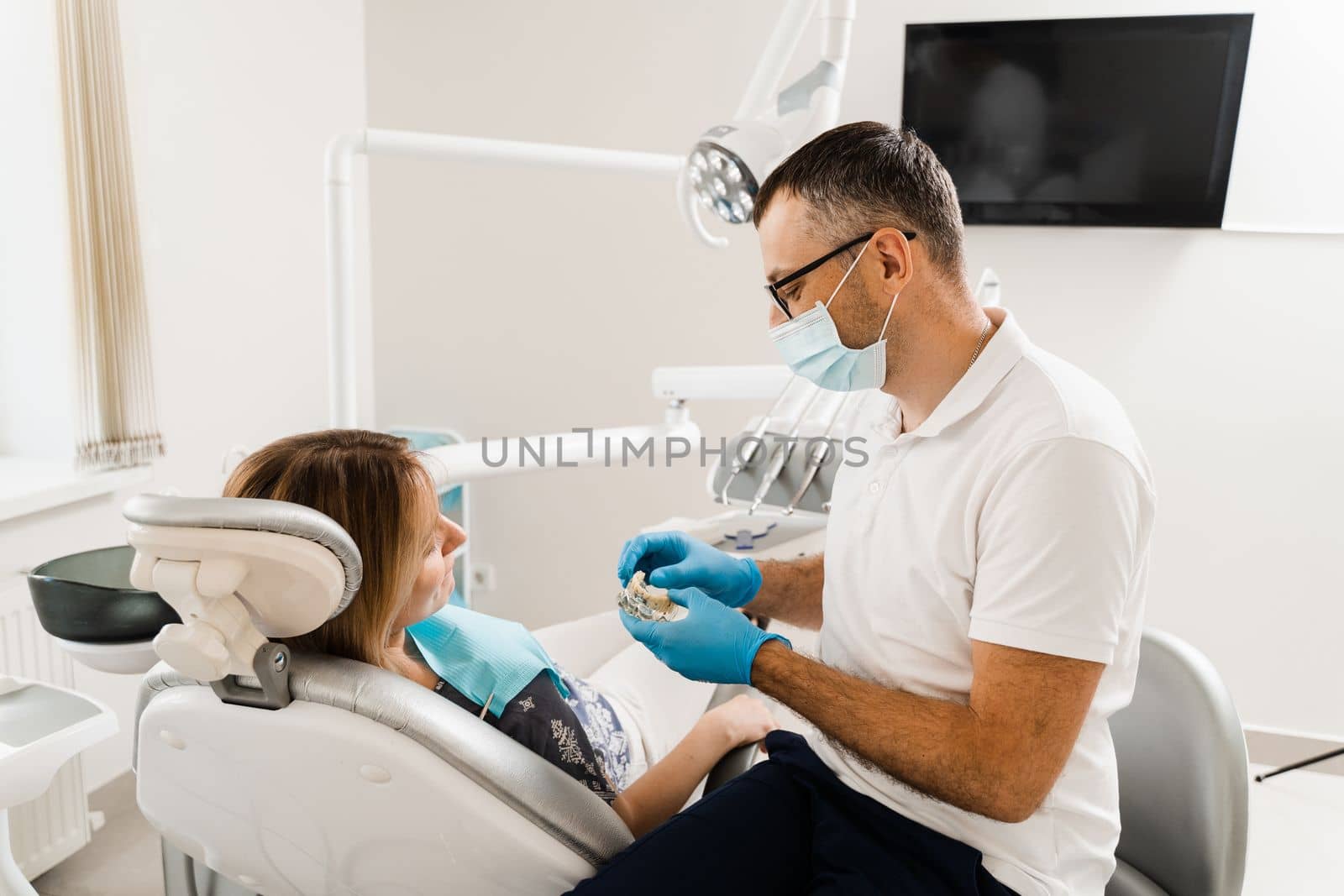 Dental prosthetics consultation with dentist for patient woman in dentistry. Doctor dentist shows artificial plastic jaw with dental implants