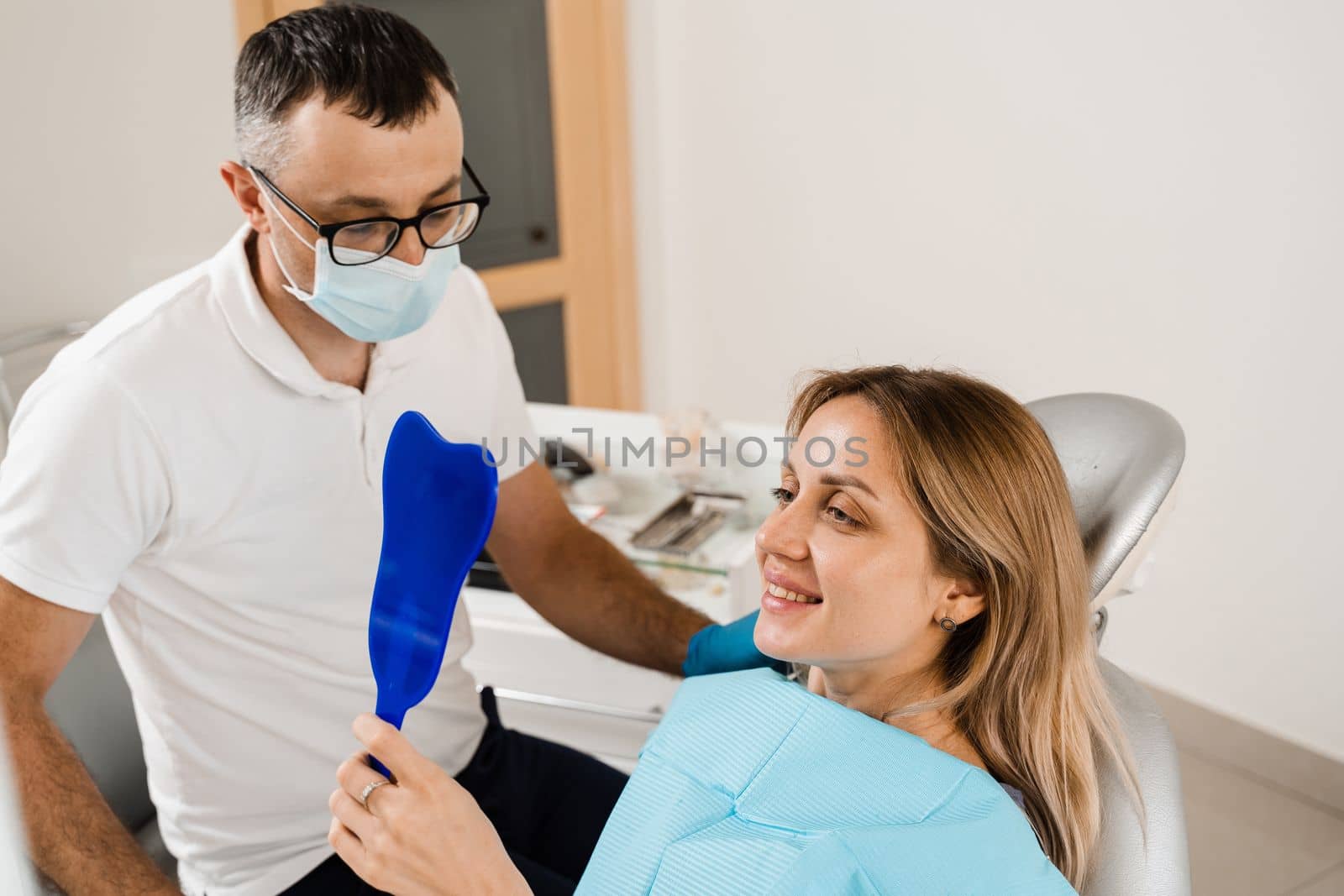 Dentist and woman patient in dentistry. Consultation with dentist at dentistry. Teeth treatment. Girl looking in the mirror at the dentist. Happy patient of dentistry. by Rabizo