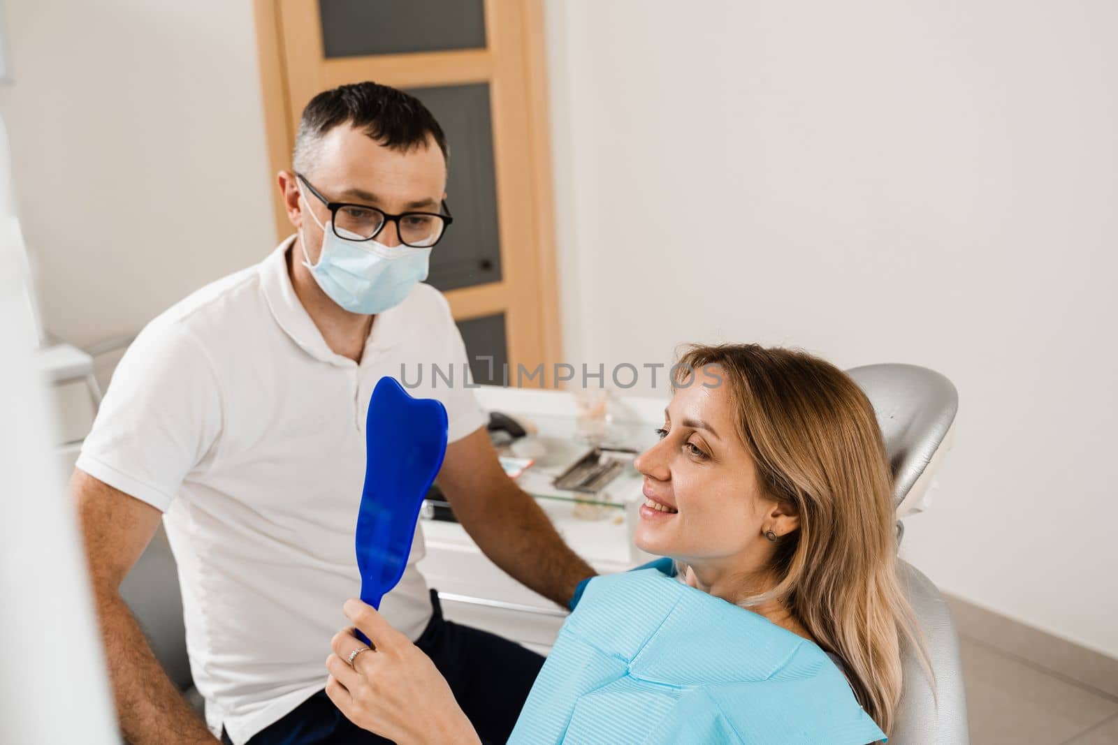 Dentist and woman patient in dentistry. Consultation with dentist at dentistry. Teeth treatment. Girl looking in the mirror at the dentist. Happy patient of dentistry. by Rabizo