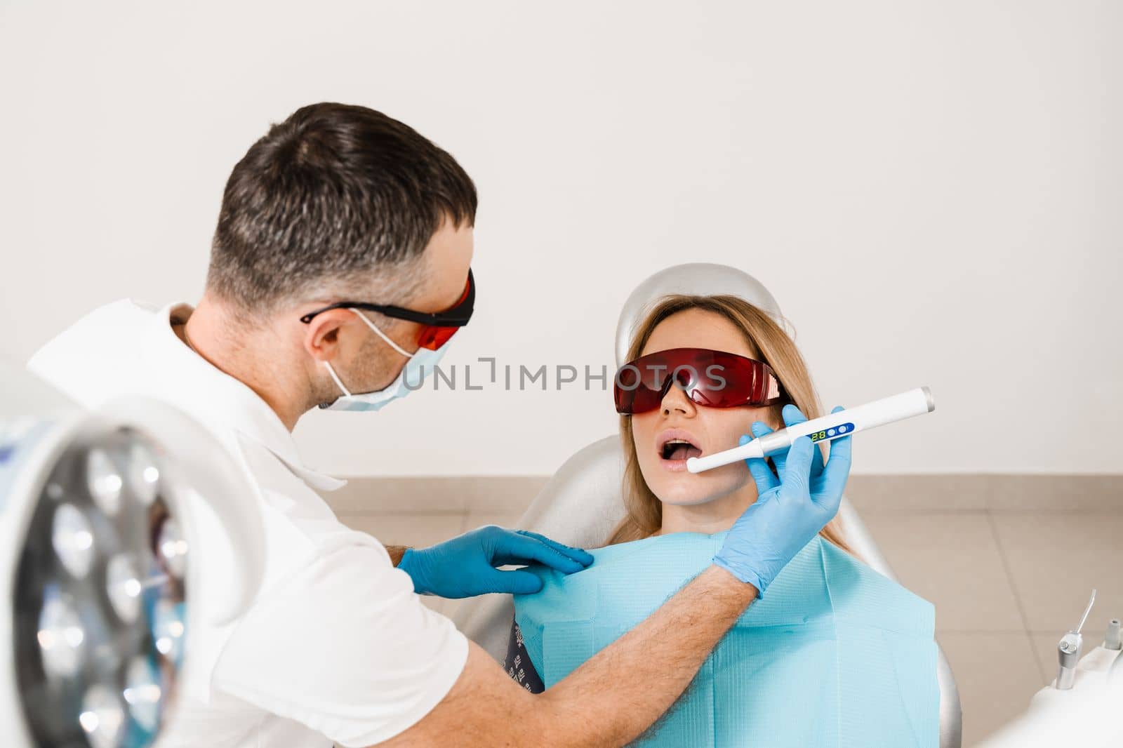 Uv illumination of photopolymer tooth filling procedure. Dentist in red protective glasses treats and removes caries in woman patient