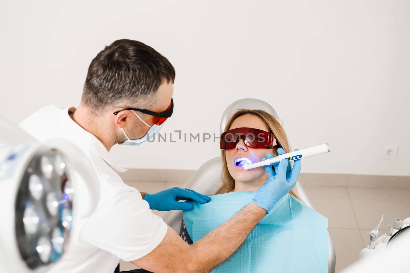 Uv illumination of photopolymer tooth filling procedure. Dentist in red protective glasses treats and removes caries in woman patient. by Rabizo