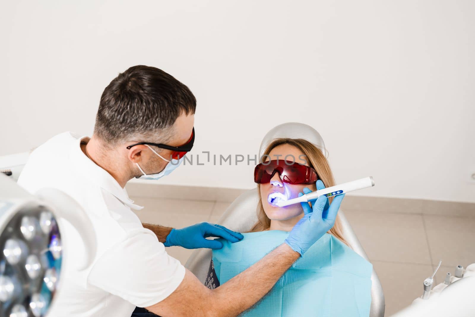 Uv illumination of photopolymer tooth filling for woman in dentistry. Dentist in red protective glasses treats and removes caries of girl patient. by Rabizo