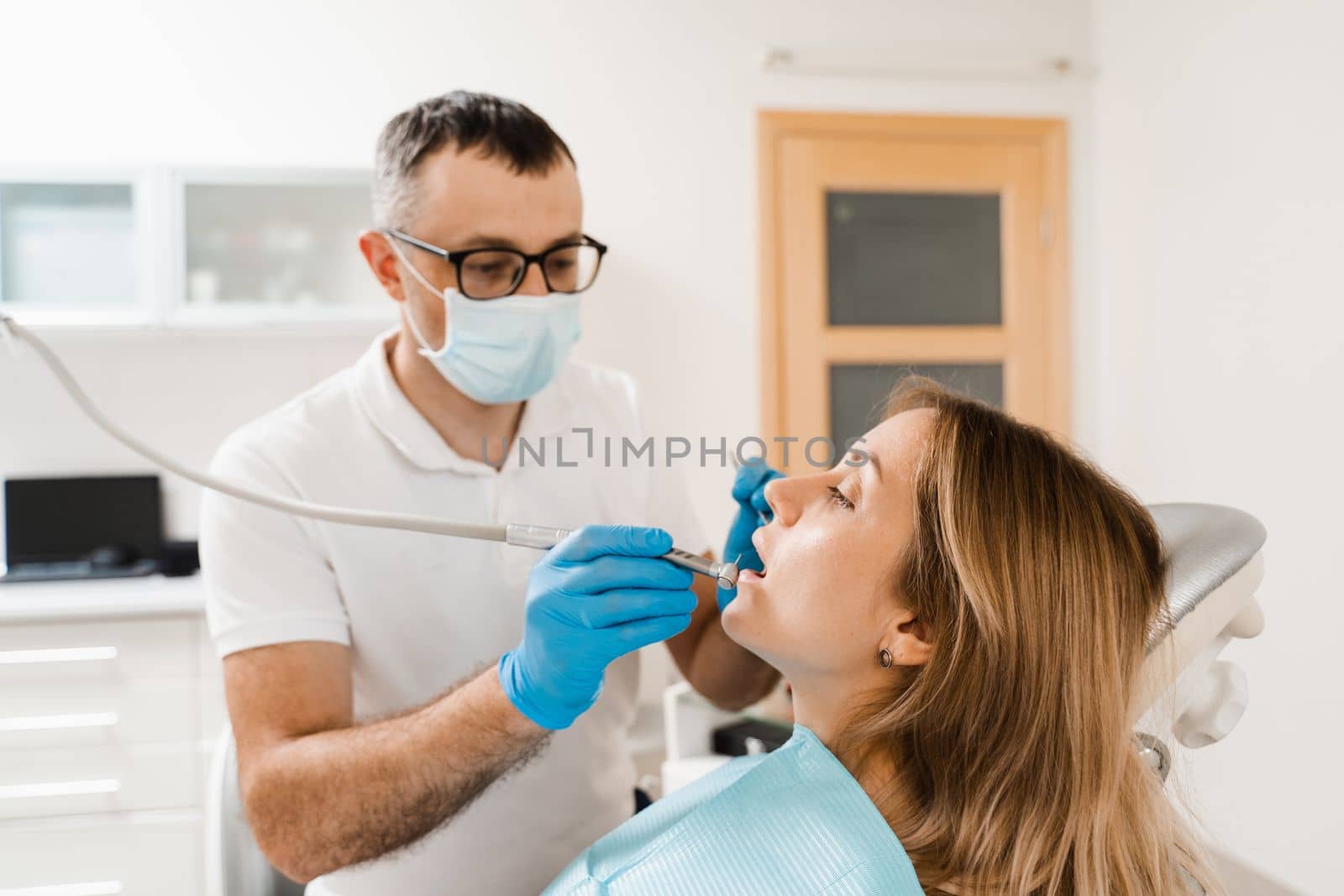 Dentist with dental drill treats woman in dentistry clinic. Dental filling for girl patient. by Rabizo