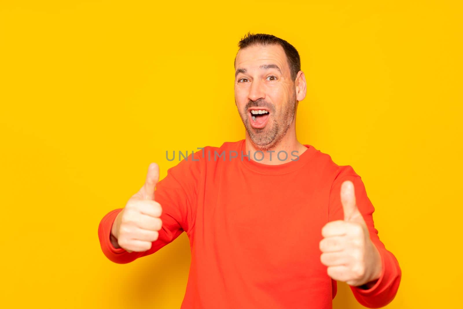 Attractive cheerful latino man with a beard wearing a red pullover standing isolated over yellow background, showing thumbs up