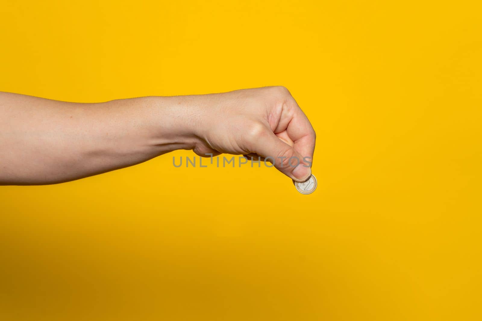 Strong man's hand ready to drop a coin isolated on a yellow background. Savings and investment concept.