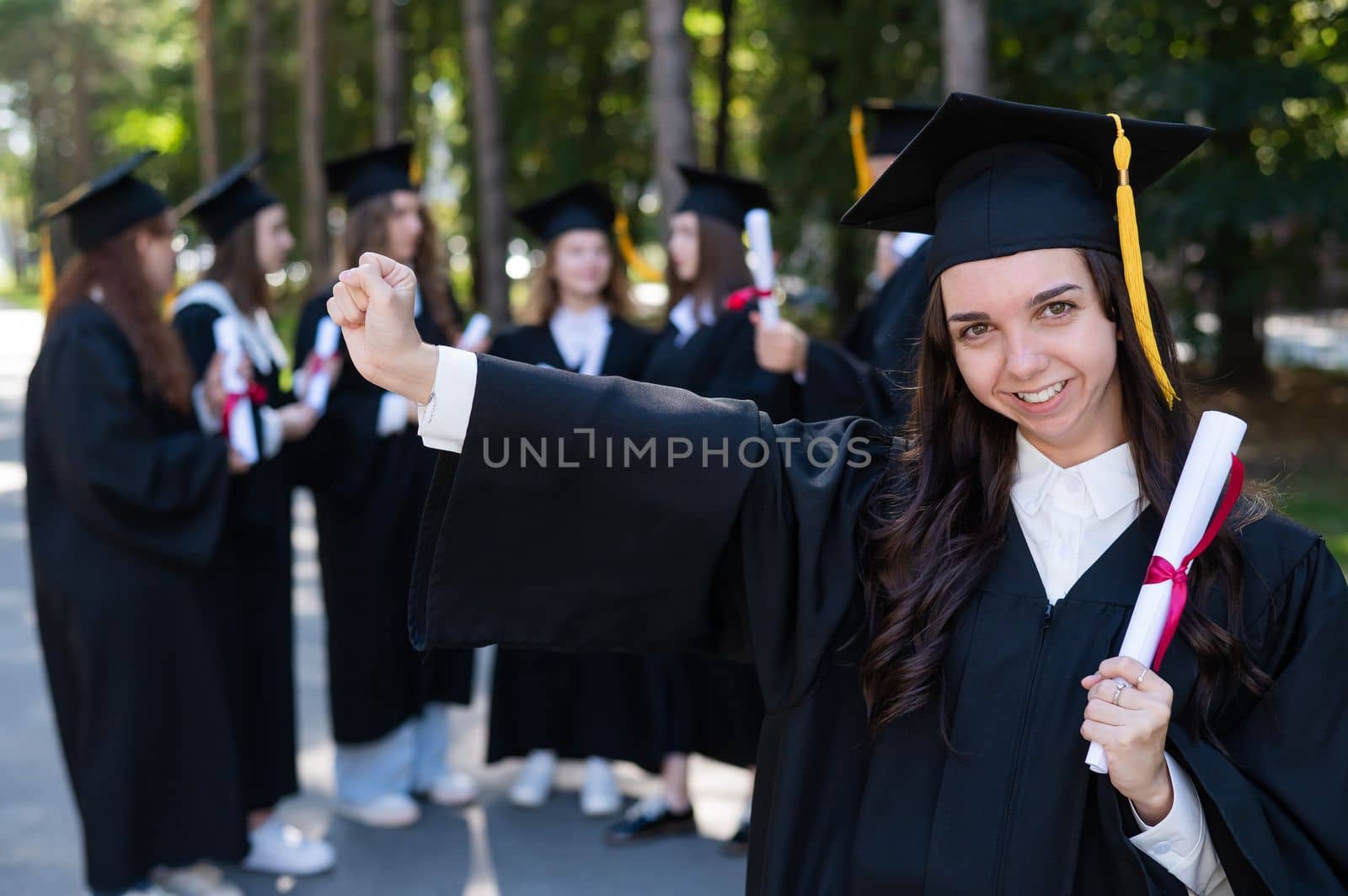 Group of happy students in graduation gowns outdoors. A young girl with a diploma in her hands in the foreground. by mrwed54