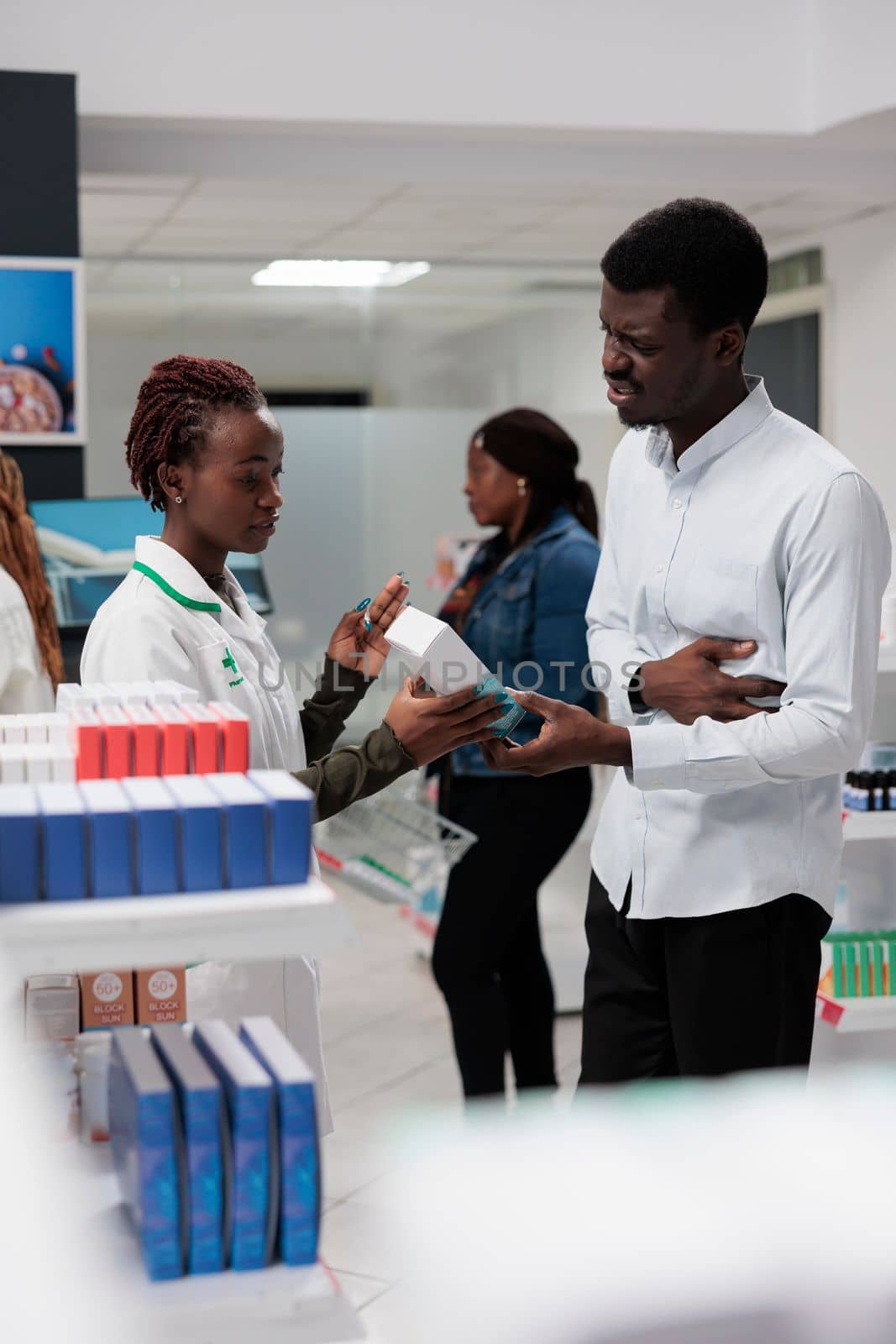 Client buying stomach pain medication, pharmacy consultant and buyer talking. African american customer with stomachache standing in drugstore, chatting with pharmacist, all black team
