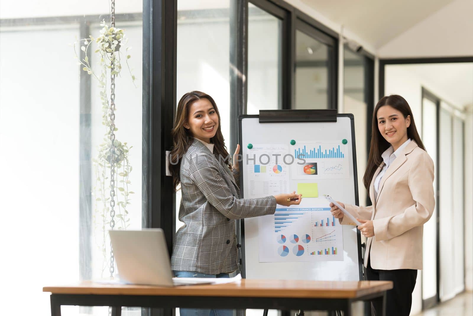 Atmosphere in the office of a startup company, two female employees are discussing, brainstorming ideas to working on summaries and marketing plans to increase sales and prepare reports to managers. by wichayada