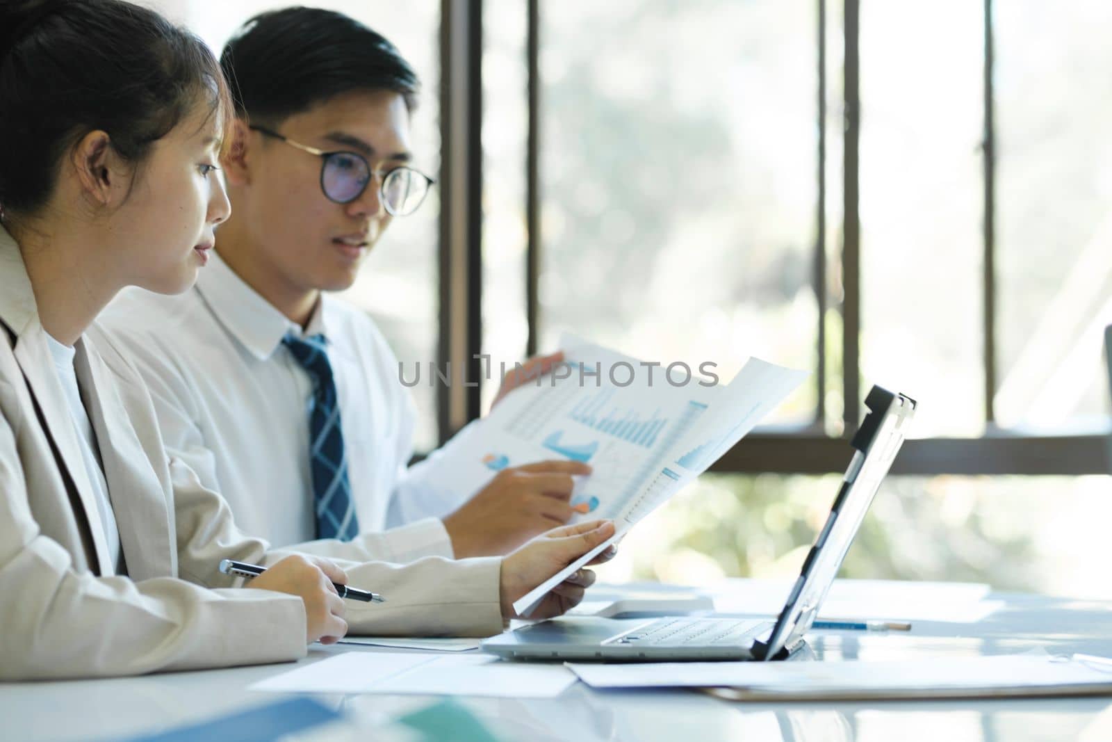 Businesspeople or colleagues are working together on project, discussing, sharing ideas, planning, and analyzing the business strategy and finance using laptop and graphs at workplace.