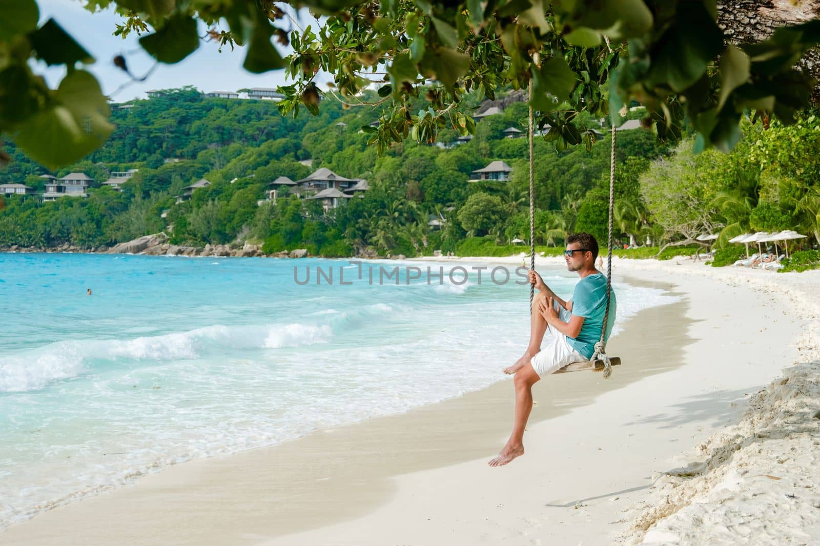 Young men relaxing in a swing on the beach of Mahe Tropical Seychelles Islands by fokkebok