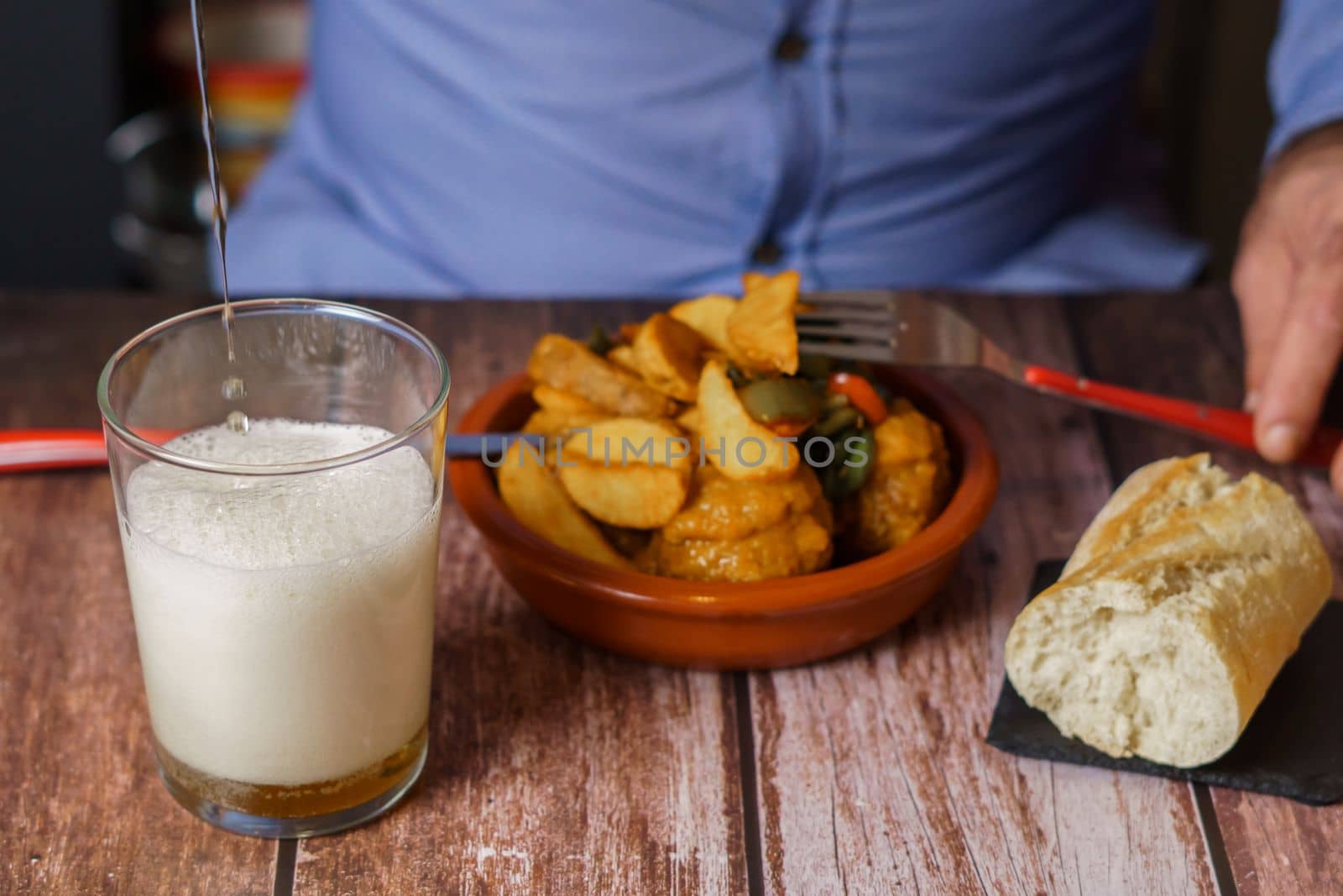 man serving beer in a glass with a meatball lid with potatoes in the background by joseantona