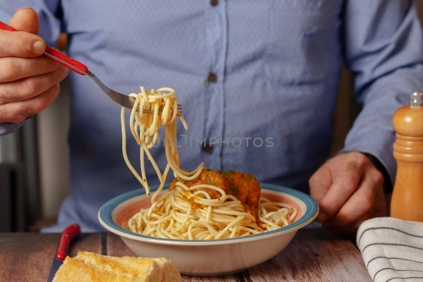 unrecognizable man in blue shirt with fork eating meatballs with spaghetti