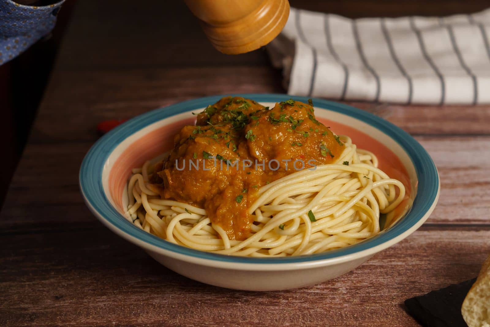 close-up of a plate of meatballs with spaghetti and parsley, pouring pepper, on a wooden table