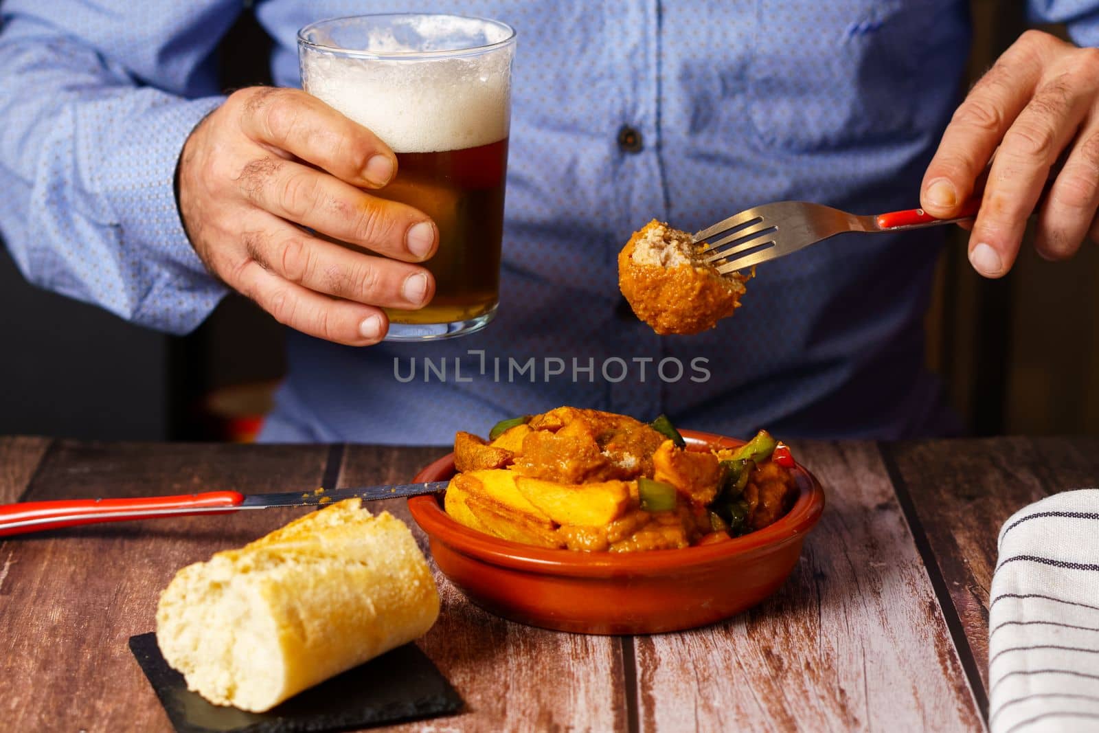 man with beard eating meatballs with spaghetti with a glass of beer in his hand by joseantona