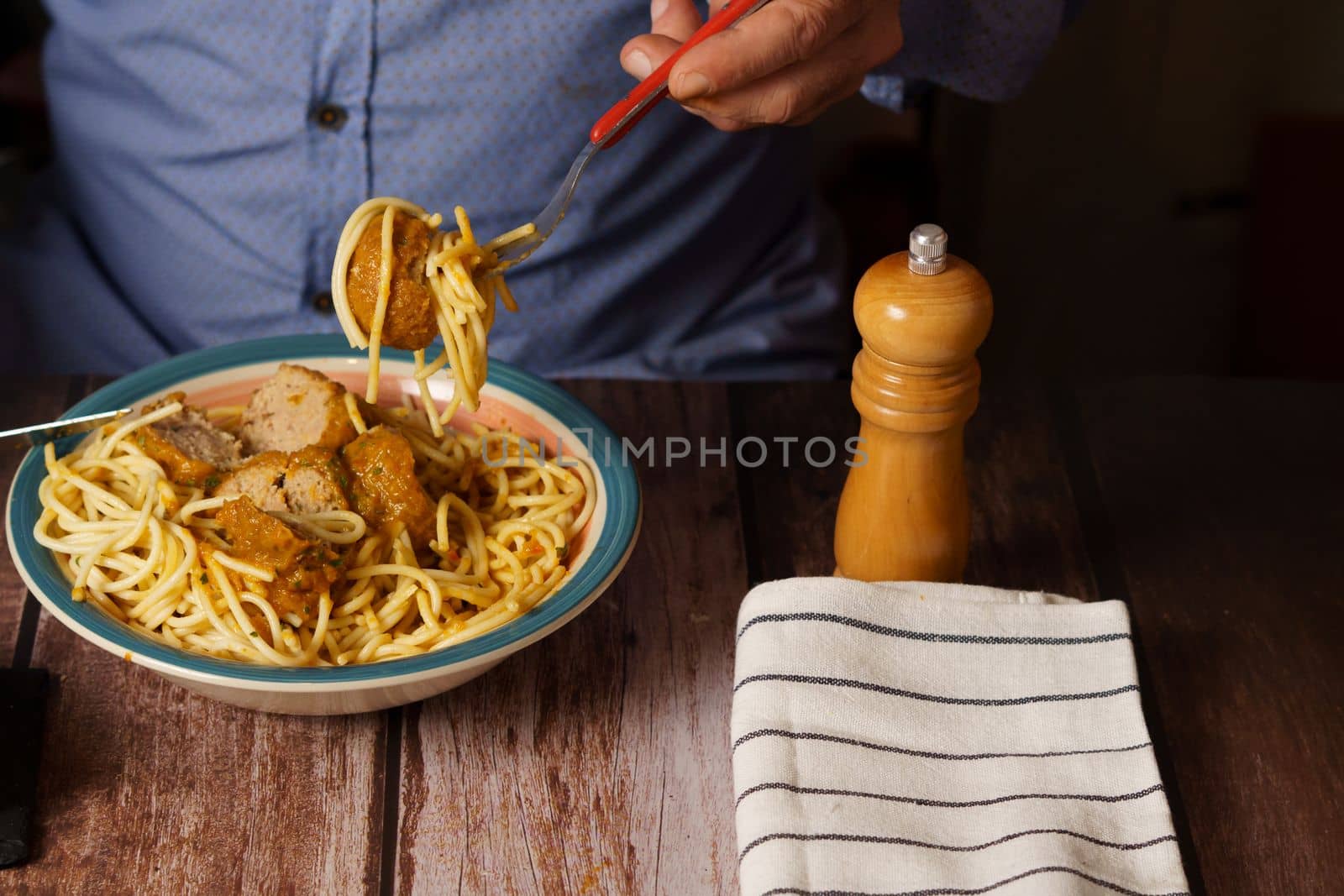 man with beard and blue shirt eating meatballs with spaghetti in a restaurant