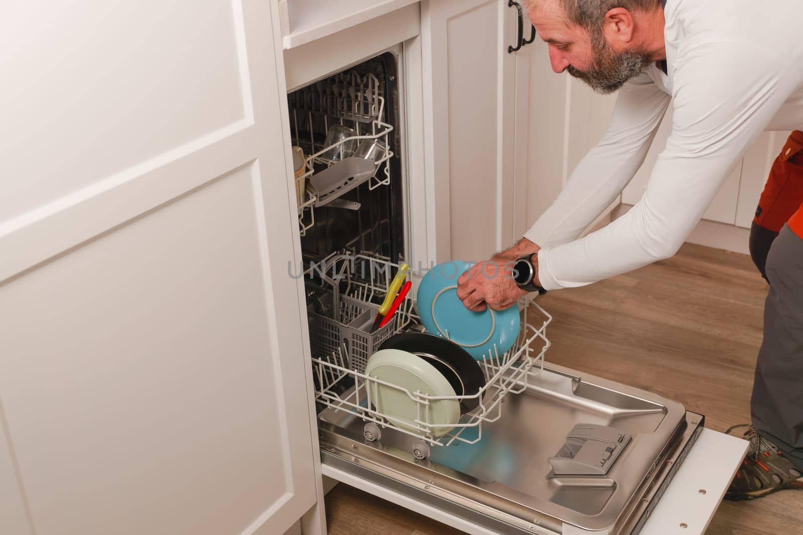 man in white t-shirt putting the dishes in the dishwasher, in the kitchen of his house