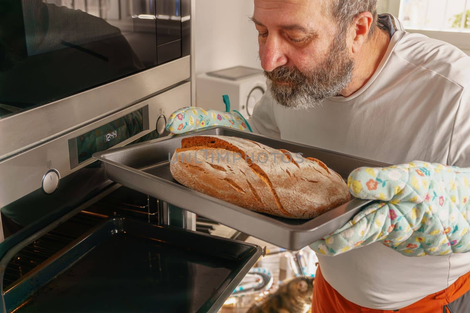 older man with beard putting bread in the oven of his house