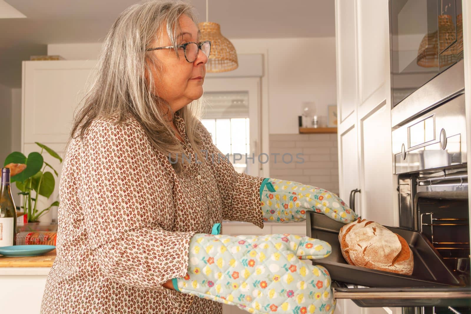 older white-haired woman putting bread in the oven in her kitchen at home