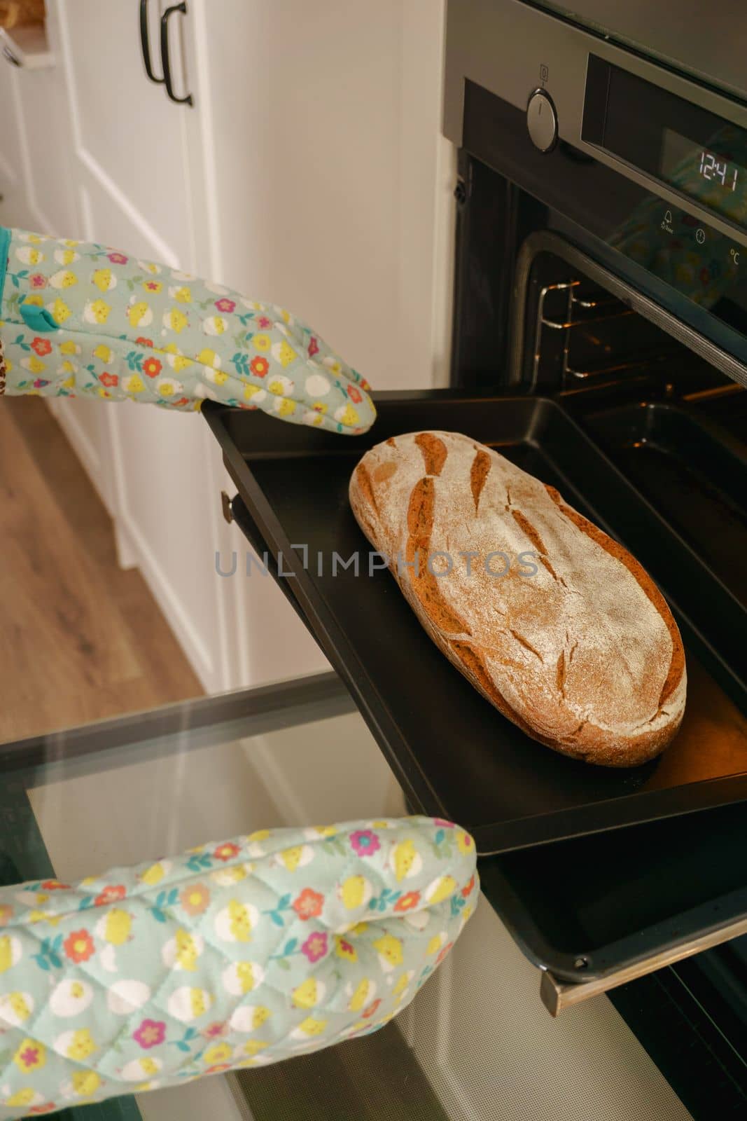 loaf of bread in the oven tray with oven mitts