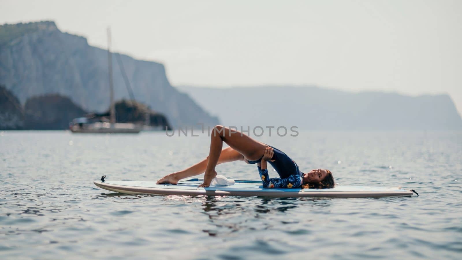 Woman sup yoga. Middle age sporty woman practising yoga pilates on paddle sup surfboard. Female stretching doing workout on sea water. Modern individual hipster outdoor summer sport activity