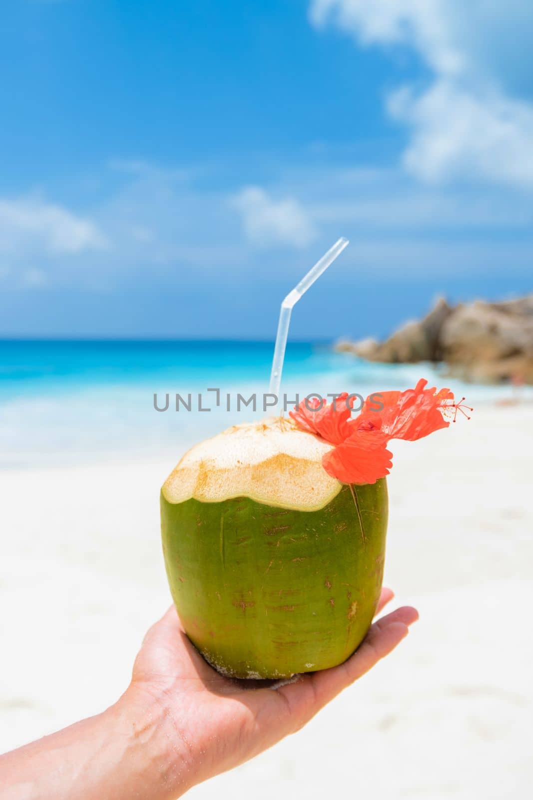 Coconut drink in palm hand on a tropical beach La Digue Seychelles Islands.