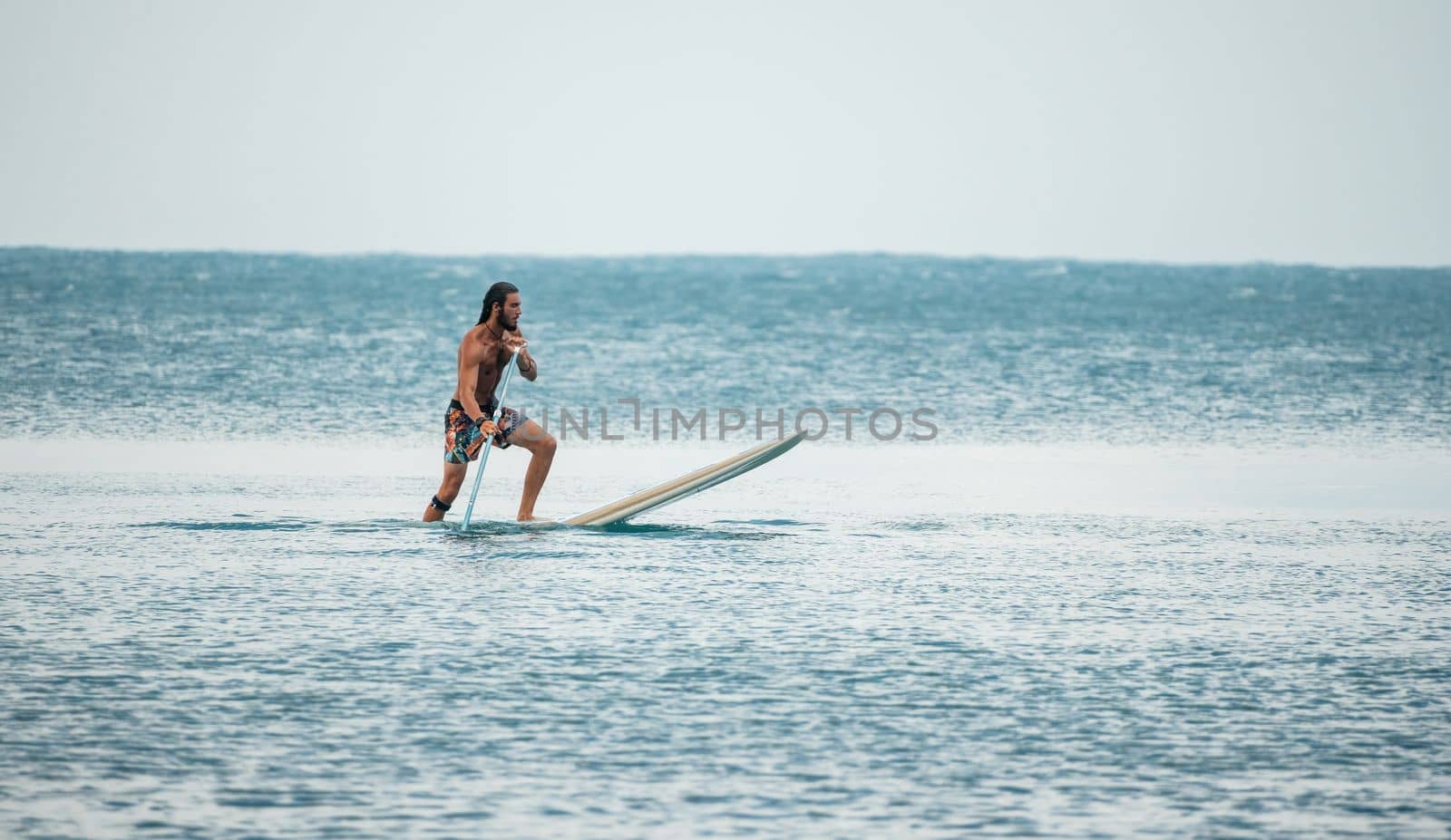 Asian man swimming in sea water and paddleboarding passing beautiful sea at summer sunset. Healthy strong male enjoy outdoor active lifestyle and water sports on holiday vacation