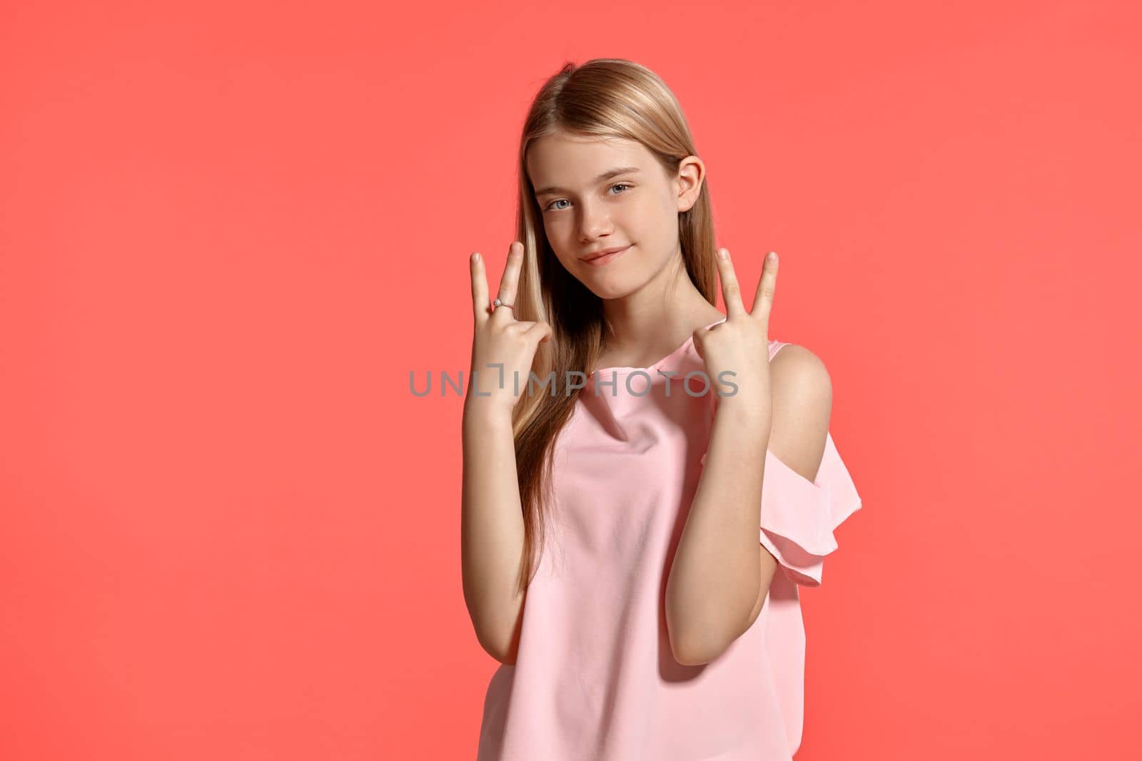 Studio portrait of a lovely blonde teenager with a long hair, in a rosy t-shirt, standing against a pink background in various poses. She expresses different emotions posing right in front of the camera, smiling and gesticulating.