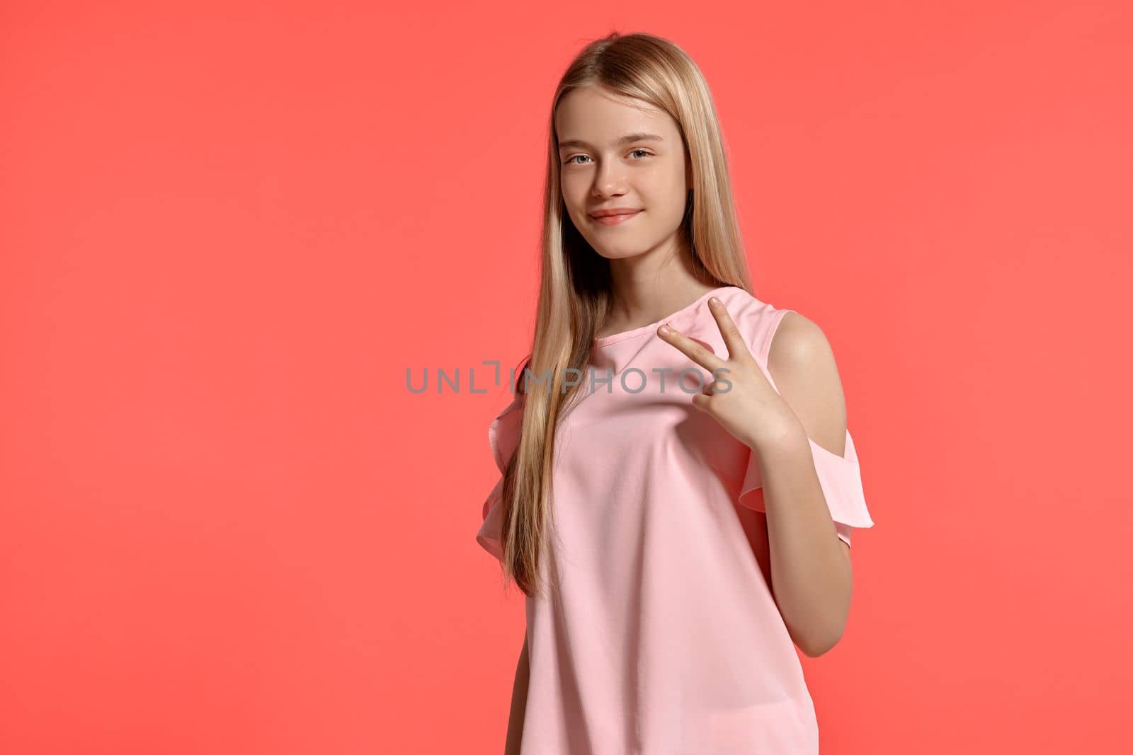 Studio portrait of an attractive blonde teenage girl with a long hair, in a rosy t-shirt, standing against a pink background in various poses. She expresses different emotions posing sideways right in front of the camera, smiling and looking happy.