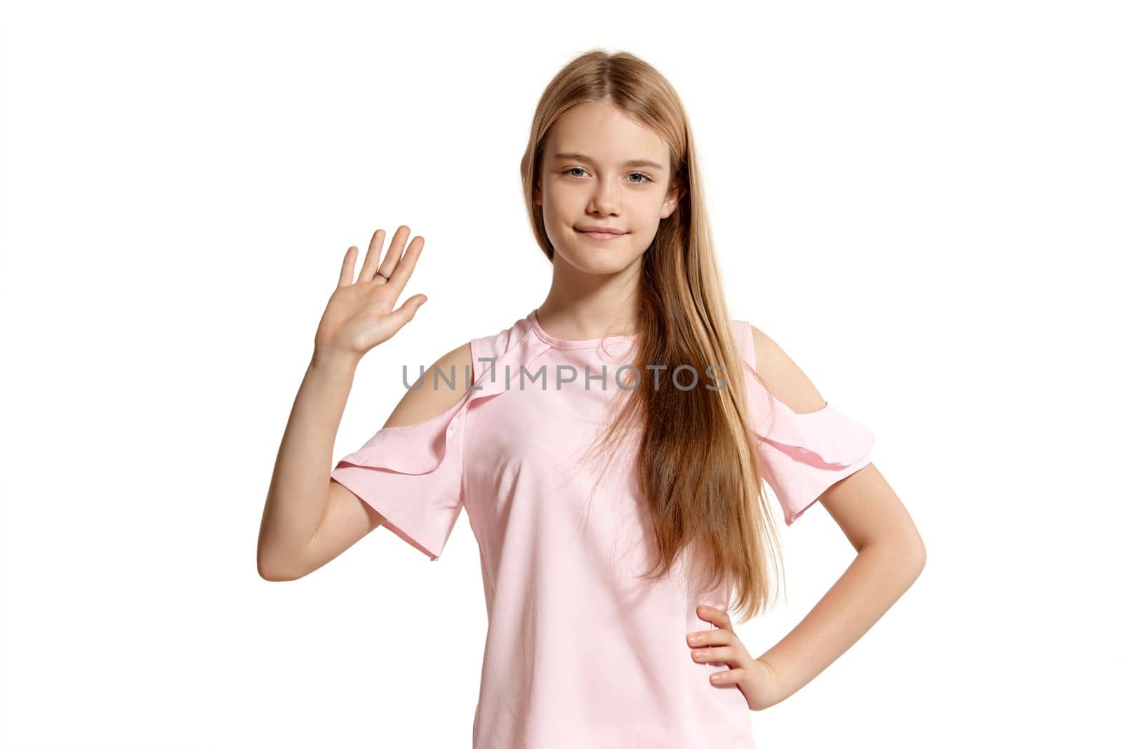 Studio portrait of a lovely blonde adolescent in a pink t-shirt isolated on white background in various poses. She expresses different emotions posing right in front of the camera, smiling and waving her hand.