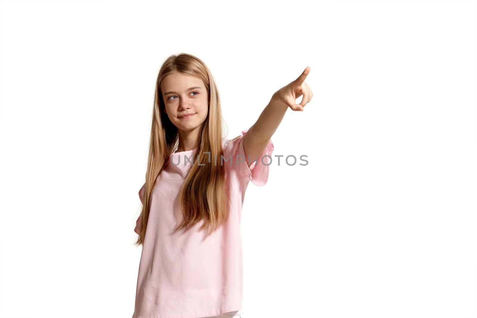 Studio portrait of a pretty blonde teenager in a pink t-shirt isolated on white background in various poses. She expresses different emotions posing right in front of the camera, looking up and pointing on something.