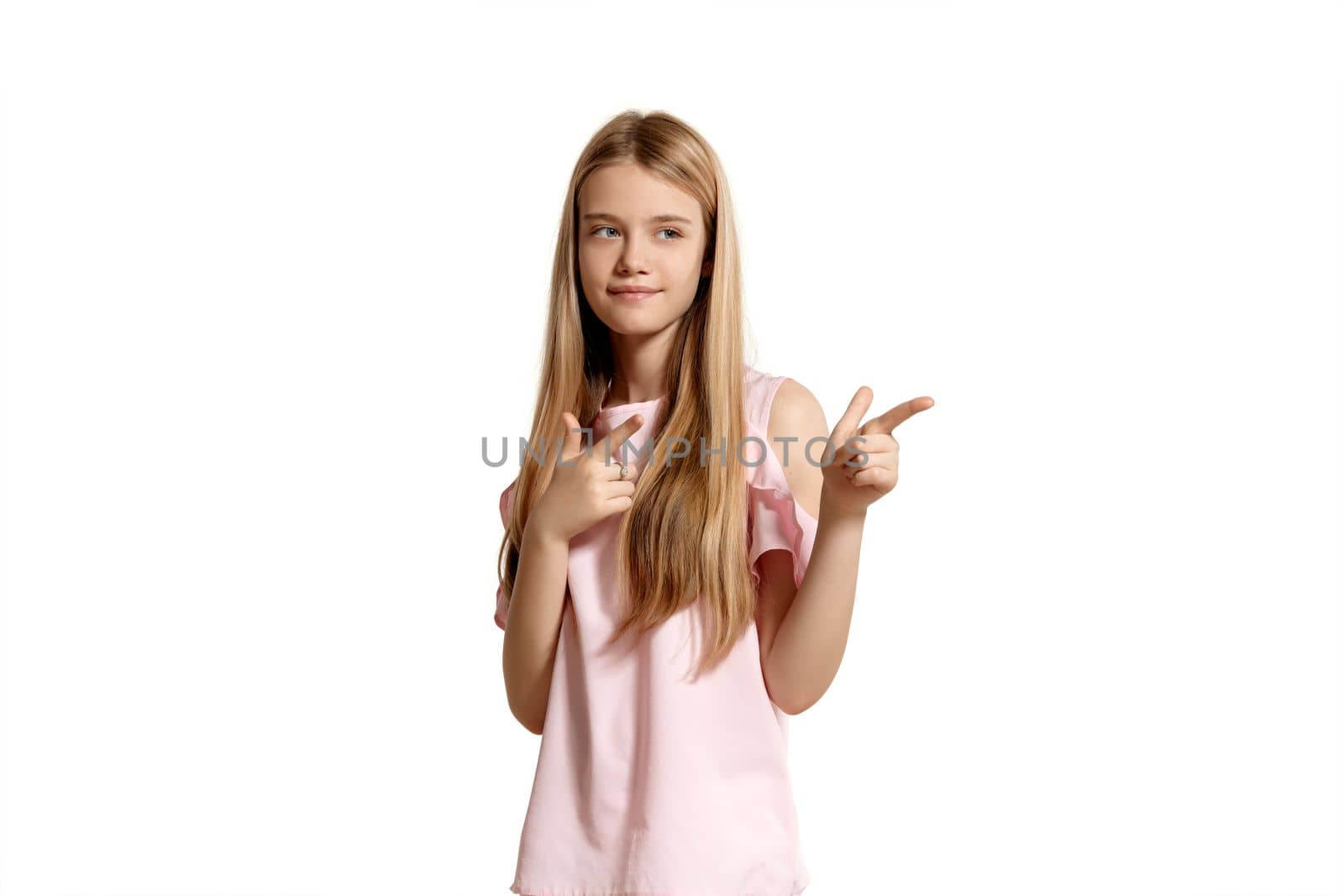 Studio portrait of a pretty blonde teenage girl in a pink t-shirt isolated on white background in various poses. She expresses different emotions posing right in front of the camera, standing sideways and pointing on something.