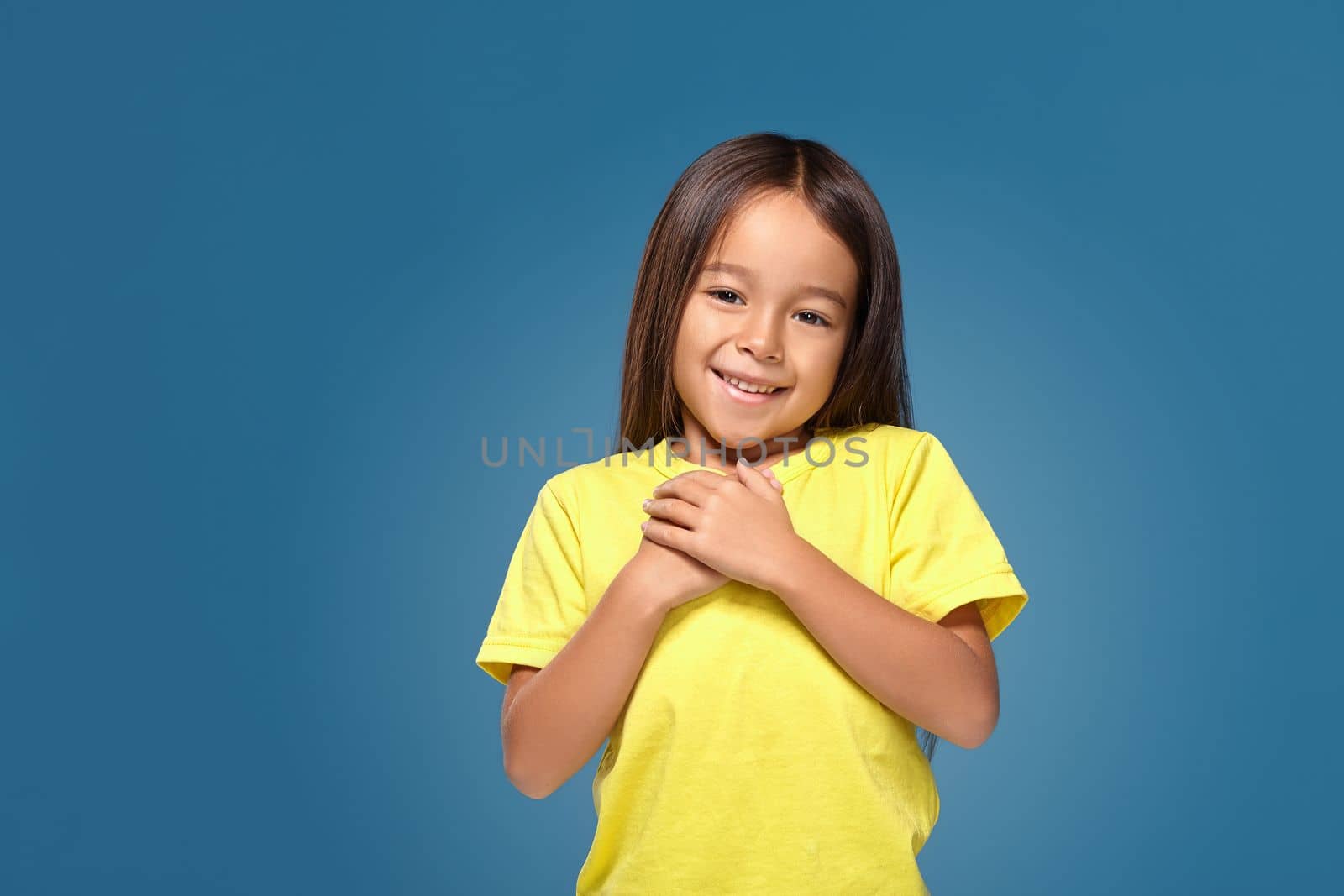 little girl in yellow t-shirt hands on her heart on the blue background