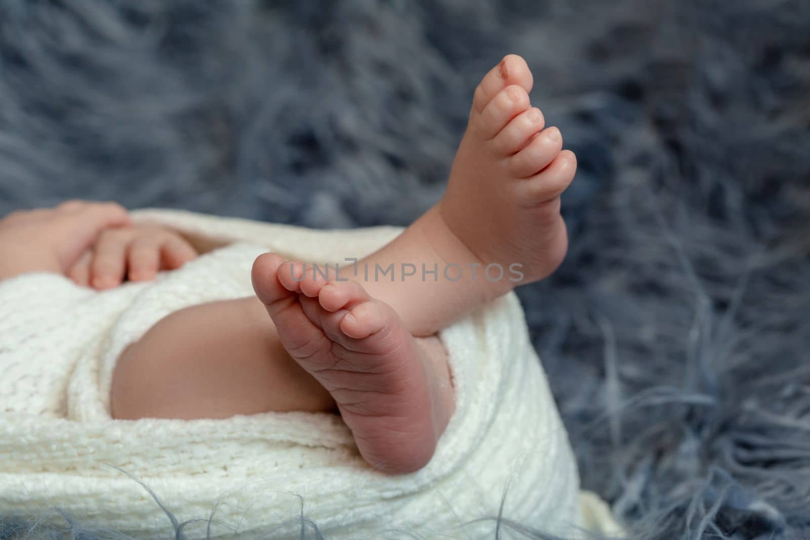 Close-up of small baby legs. The sleeping Newborn boy under a white knitted blanket lies on the blue fur. by nazarovsergey