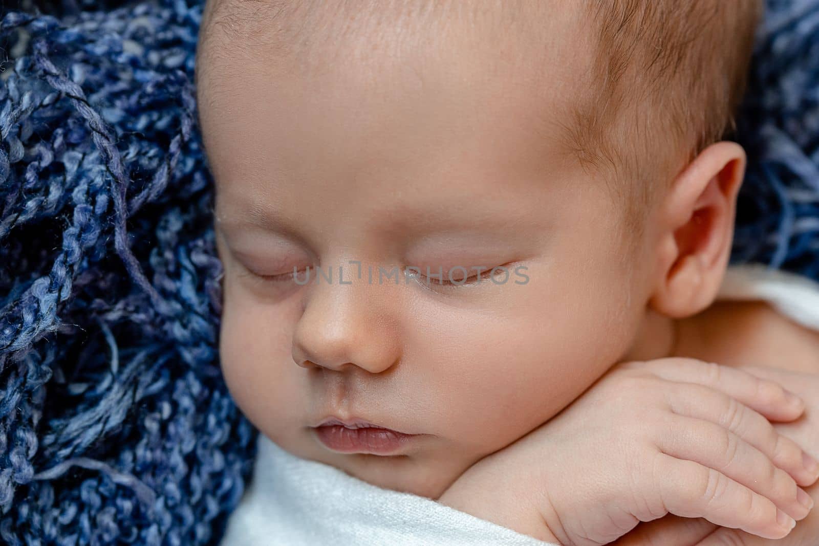 Newborn - baby, face close-up. The sleeping Newborn boy under a white knitted blanket lies on the blue fur. by nazarovsergey