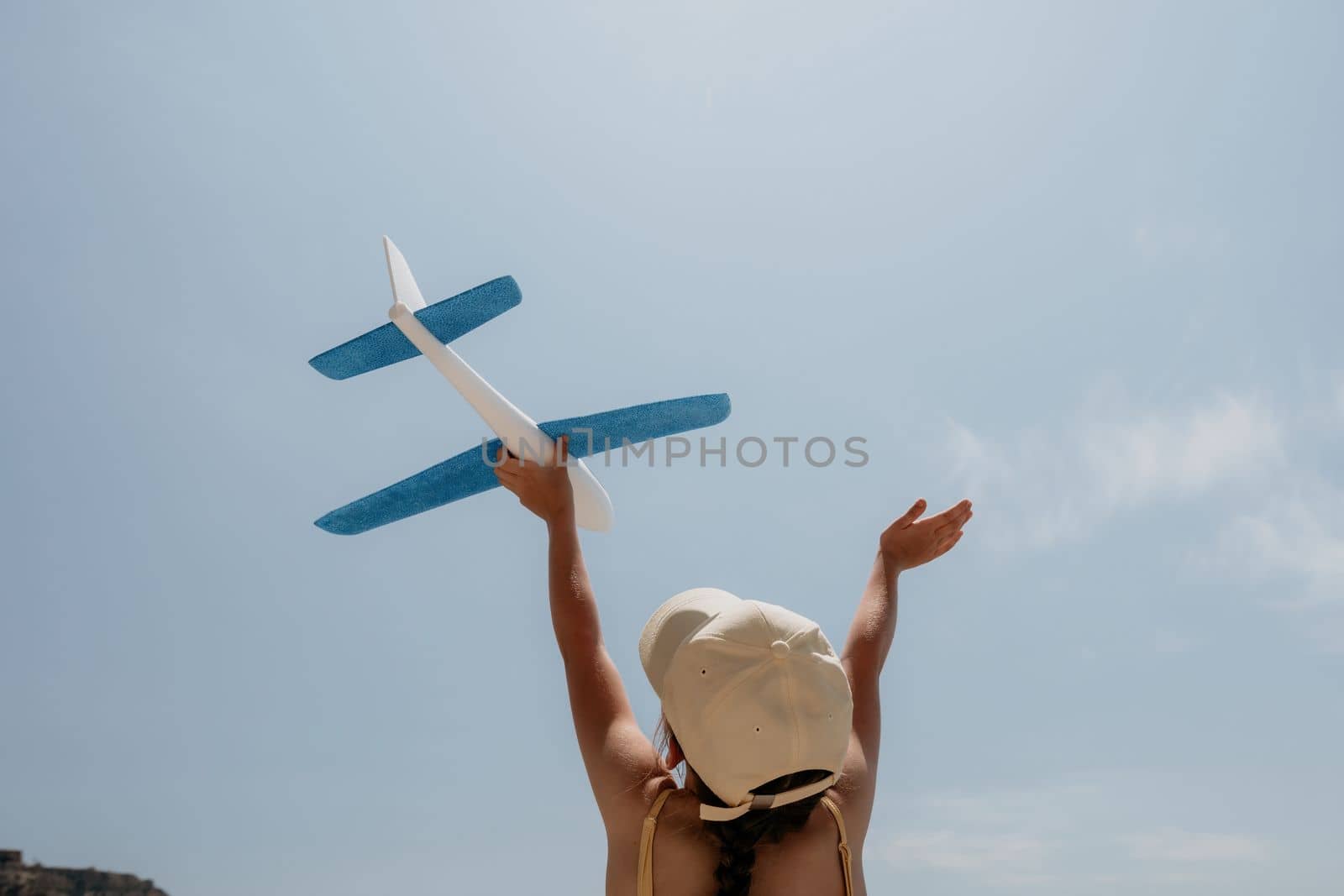 Kid playing with toy airplane. Children dream of travel by plane. Happy child girl has fun in summer vacation by sea and mountains. Outdoors activities at background of blue sky. Lifestyle moment
