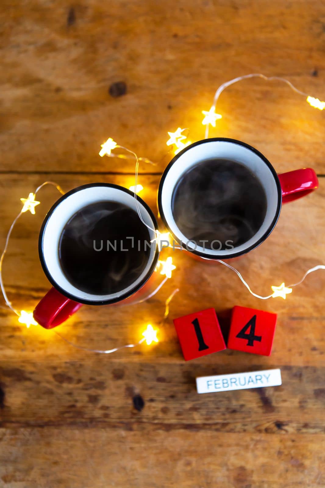 Two cups of coffee in red cups on a background of garlands. Postcard with date and month. Morning breakfast for Valentine's Day. View from above